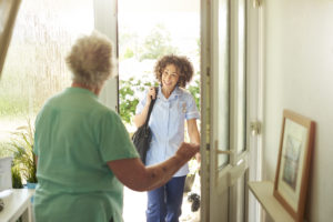 Home setting where an older woman greets a young female caregiver walking through the door