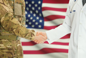 Military personnel shaking hands with medical professional with US flag in background
