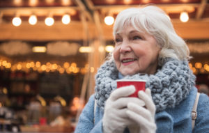 Older woman outside with holiday lights enjoying a warm drink